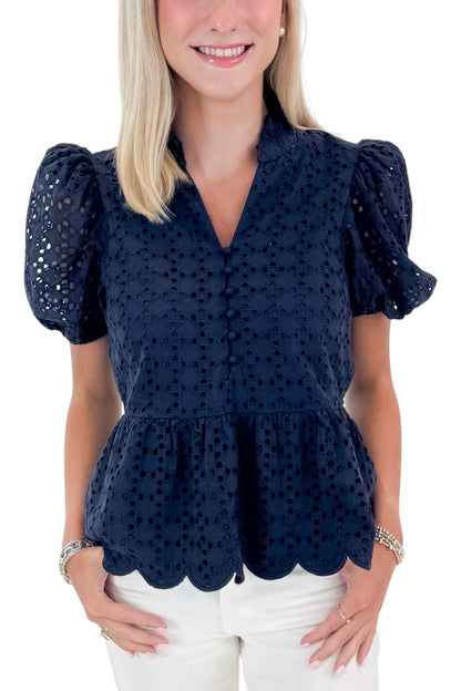 Front detail view of woman wearing Navy Short Sleeve Peplum Eyelet Top with jeans against white studio background.