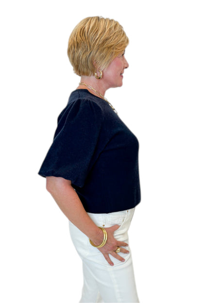 Side view of woman wearing Swagger Boutique’s Navy Short Sleeve Sweater with jeans against white studio background.