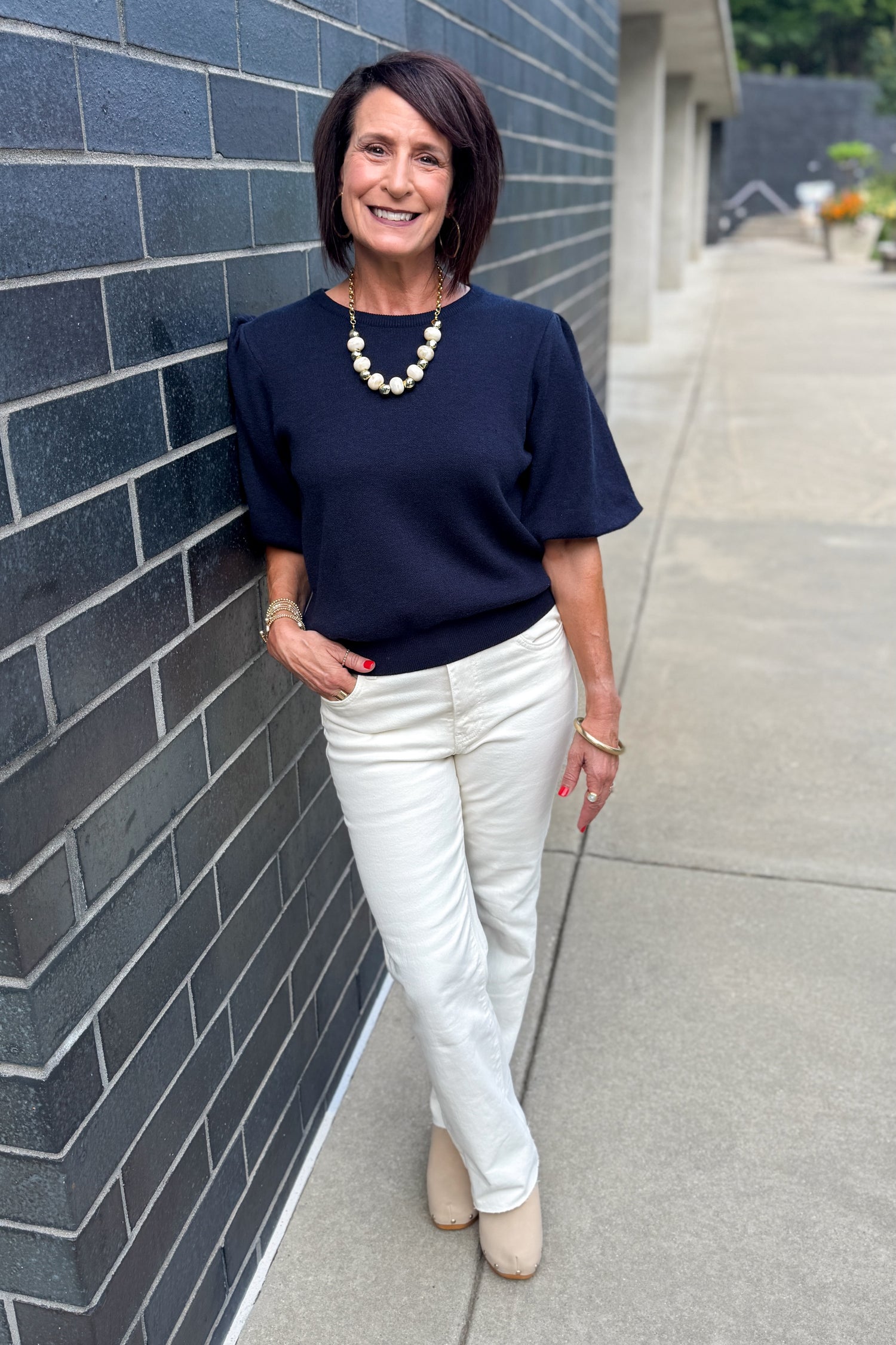 Front view of woman wearing Swagger Boutique’s Navy Short Sleeve Sweater with jeans standing outside by a brick wall.