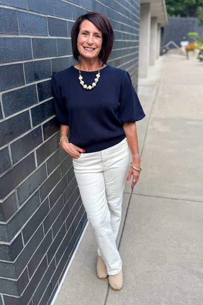 Front view of woman wearing Swagger Boutique’s Navy Short Sleeve Sweater with jeans standing outside by a brick wall.