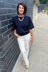 Front view of woman wearing Swagger Boutique’s Navy Short Sleeve Sweater with jeans standing outside by a brick wall.