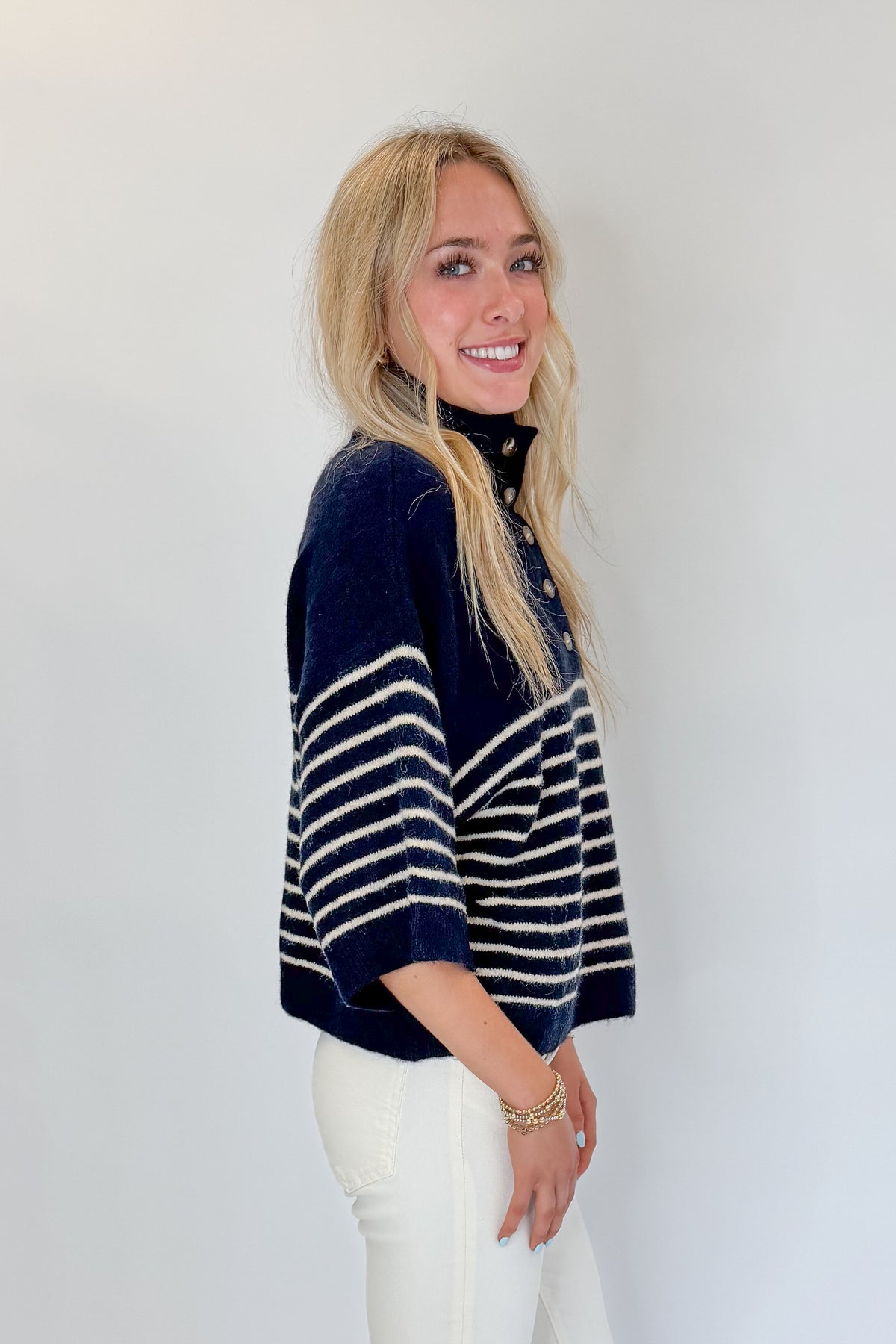 Side view of woman wearing Swagger Boutique’s Navy Striped 3/4 Sleeve Sweater by Entro with jeans against white studio background.