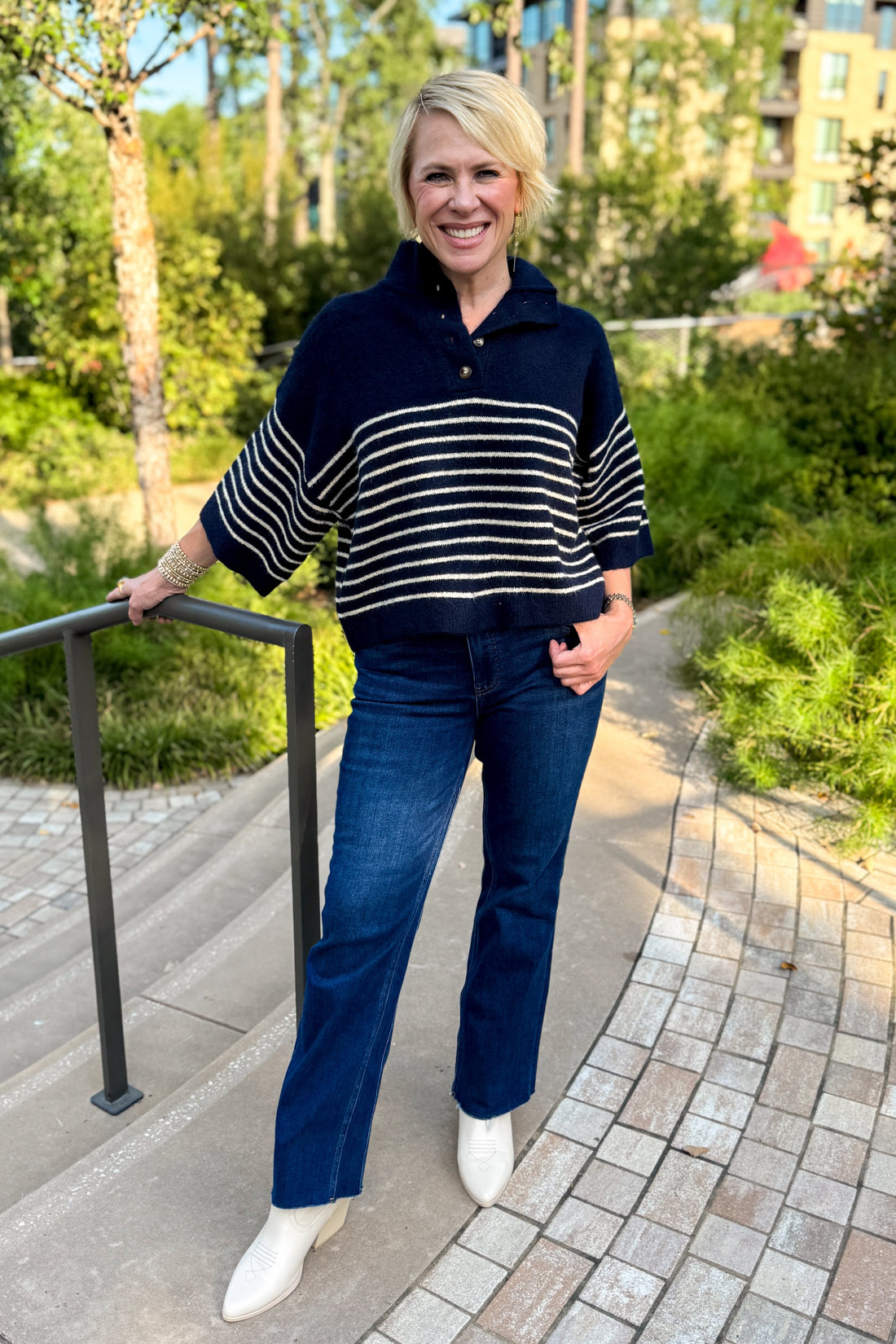 Front view of women wearing Swagger Boutique’s navy striped 3/4 sleeve sweater standing outside by a garden.