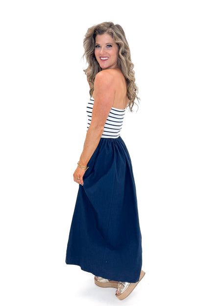 Side view of woman wearing Swagger Boutique’s Navy Striped Maxi Dress with sandals against white studio background.