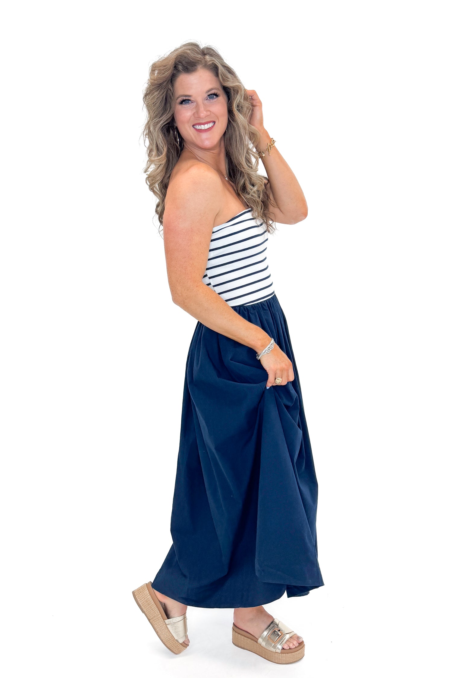 Side view of woman wearing Swagger Boutique’s Navy Striped Maxi Dress with sandals against white studio background.