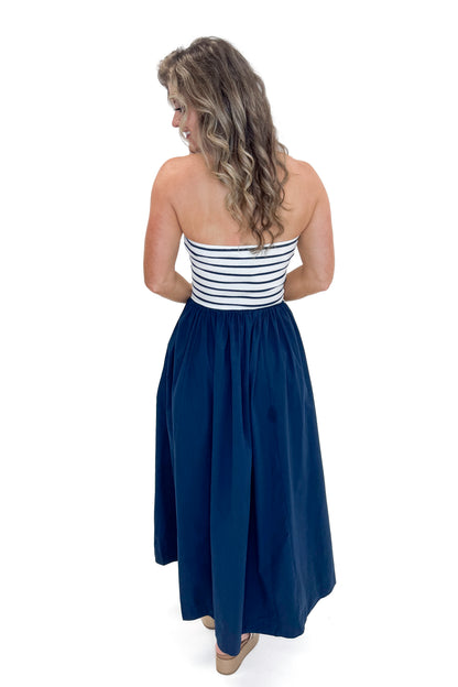 Back view of woman wearing Swagger Boutique’s Navy Striped Maxi Dress with sandals against white studio background.