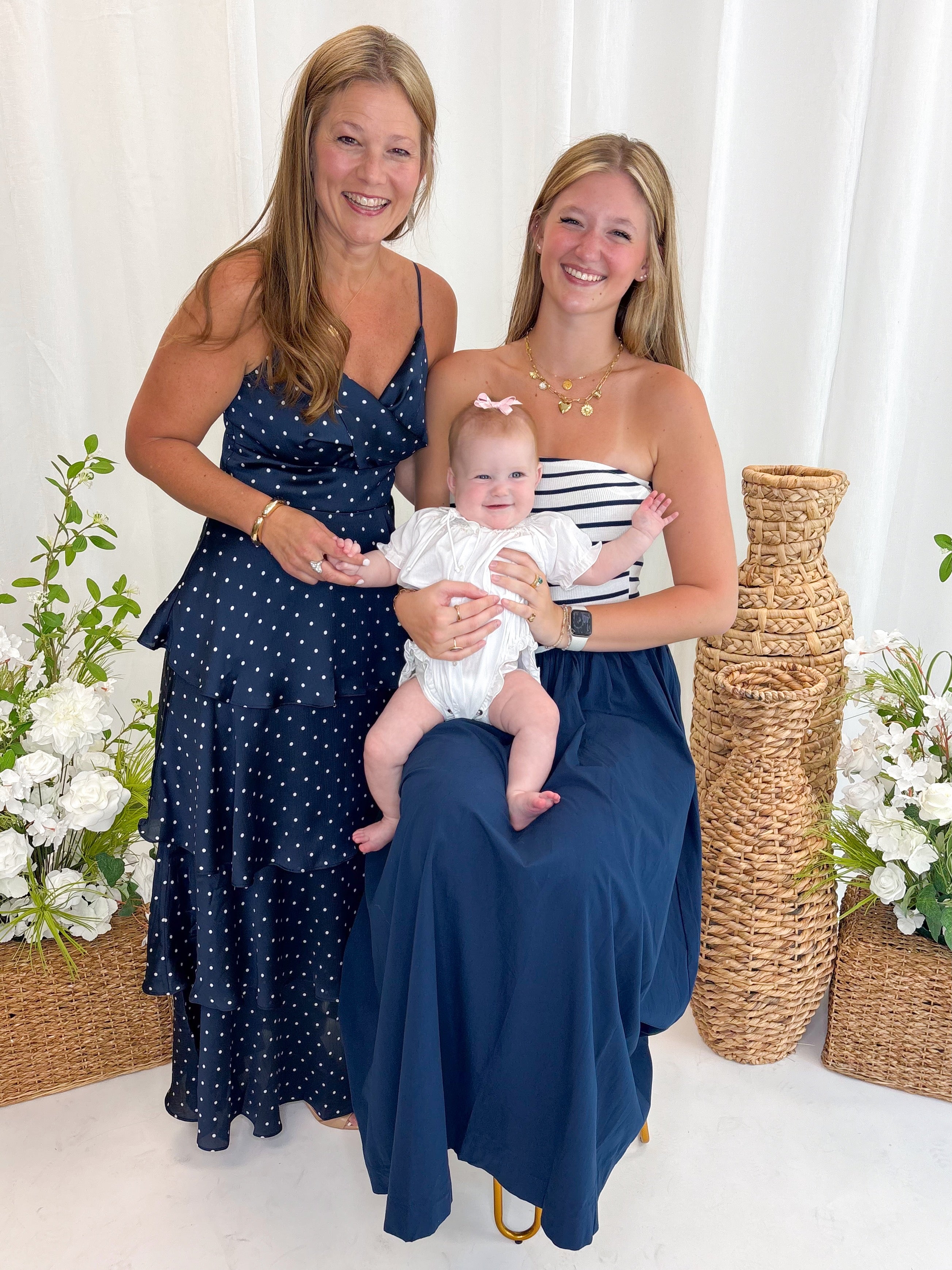 Front view of woman wearing Swagger Boutique’s Navy Striped Maxi Dress and Navy Polka Dot Tiered Maxi Dress with sandals against white decorative background.