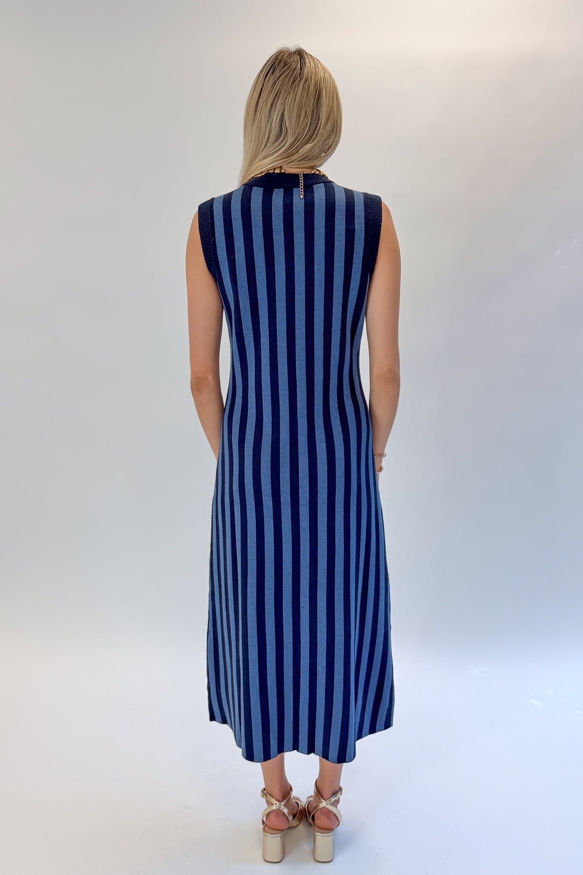Back view of woman wearing Swagger Boutique’s Navy &amp; Blue Striped Midi Dress with heels against white studio background.