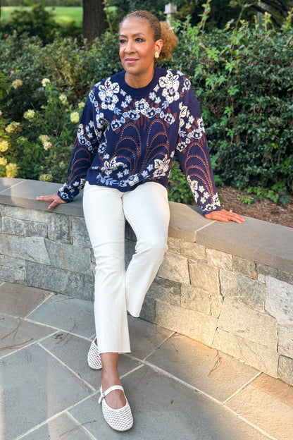 Front view of woman wearing Swagger Boutique’s Navy &amp; Brown Printed Sweater by THML with jeans sitting on a stone wall outside.