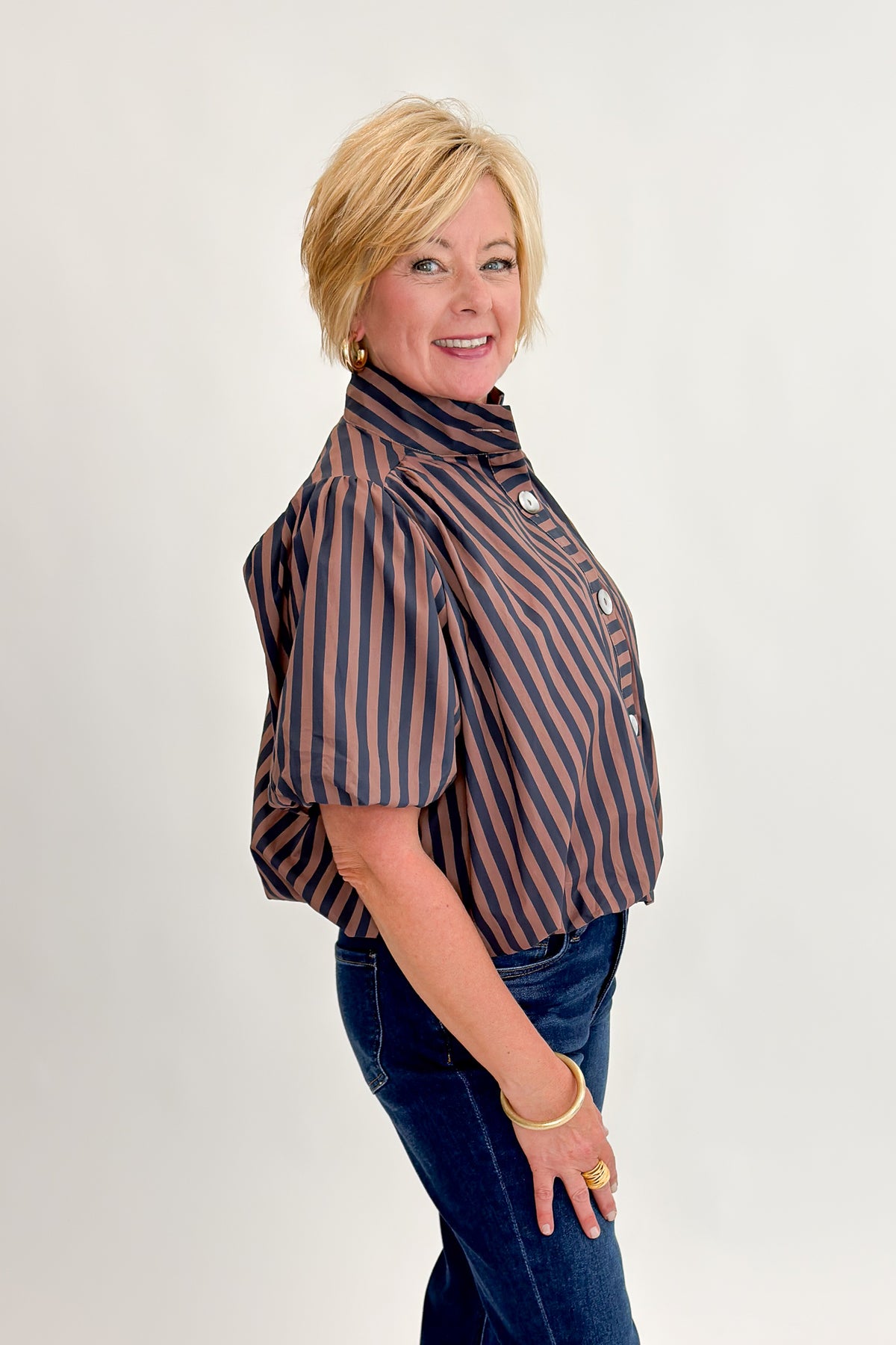 Side view of woman wearing Swagger Boutique’s Navy &amp; Brown Striped Bubble Hem Top with jeans against white studio background.