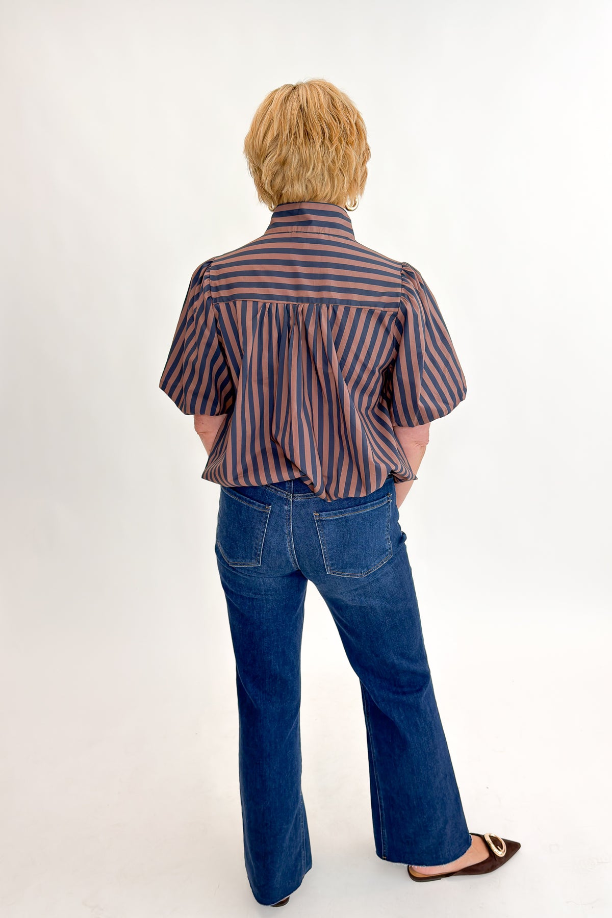 Back view of woman wearing Swagger Boutique’s Navy &amp; Brown Striped Bubble Hem Top with jeans against white studio background.