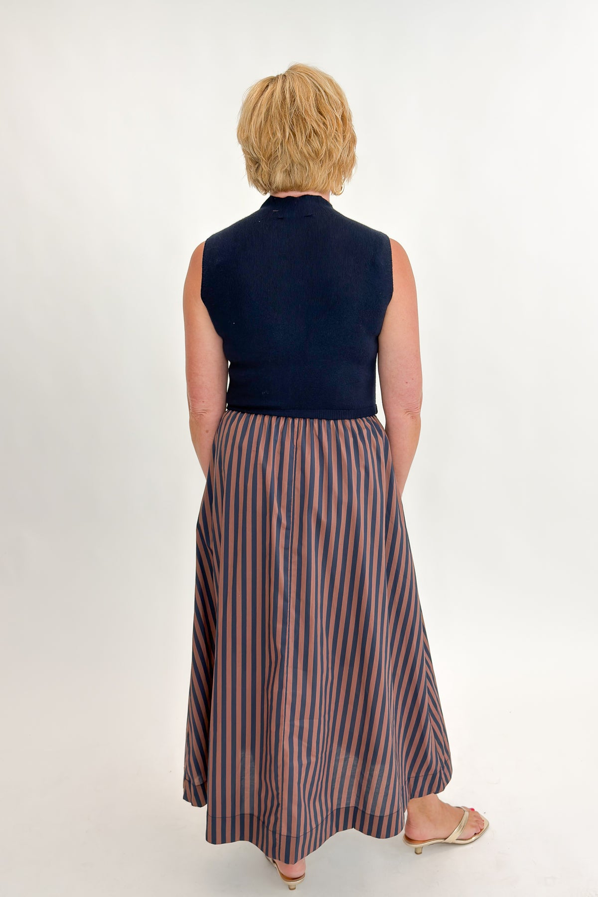 Back view of woman wearing Swagger Boutique’s Navy &amp; Brown Striped Layered Mock Neck Midi Dress against white studio background.