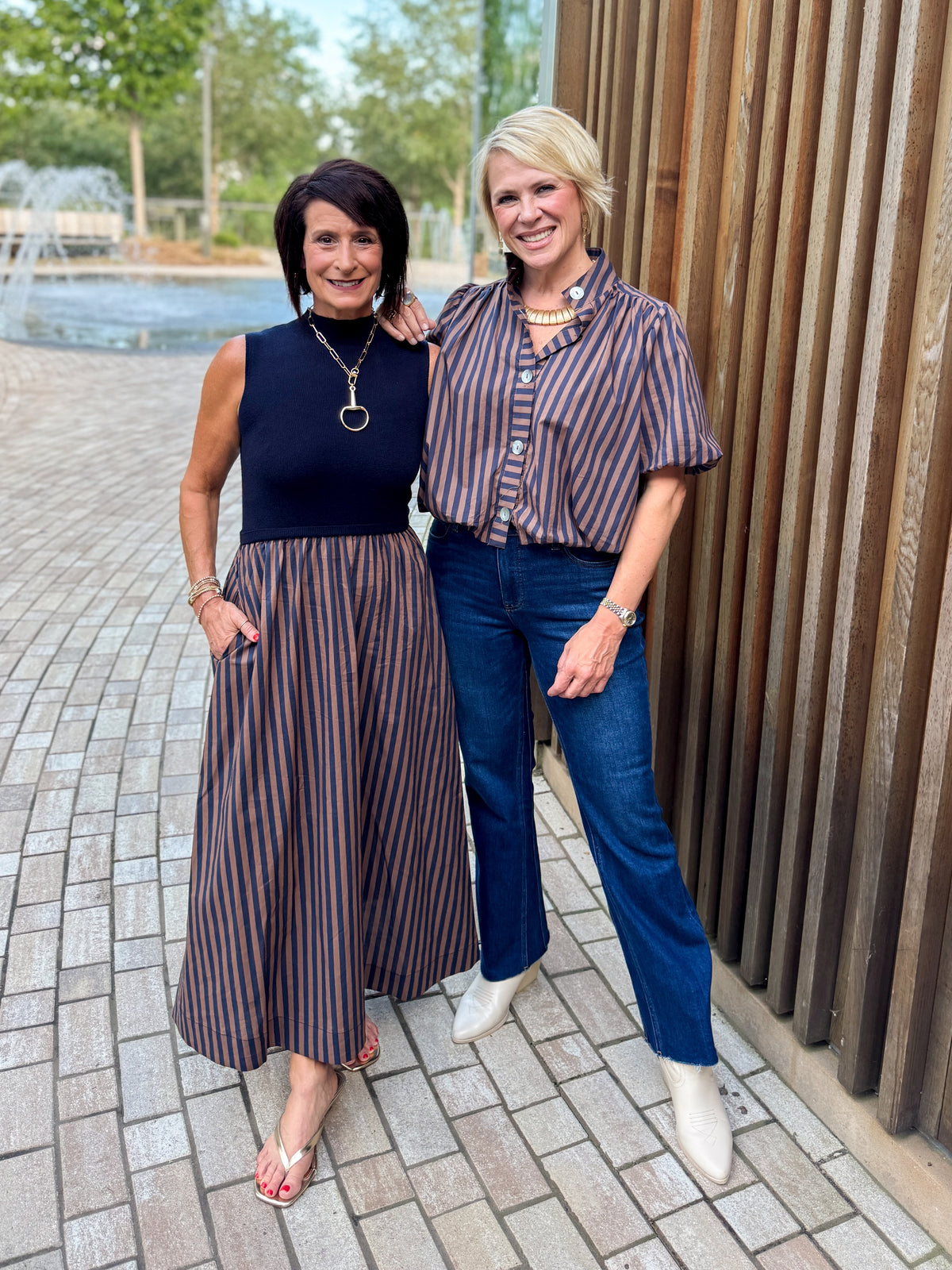 Front view of women wearing Swagger Boutique’s Navy &amp; Brown Striped Layered Mock Neck Midi Dress and stripe top standing by a fountain outside.