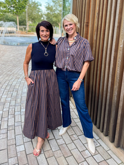 Front view of women wearing Swagger Boutique’s Navy &amp; Brown Striped Layered Mock Neck Midi Dress and stripe top standing by a fountain outside.