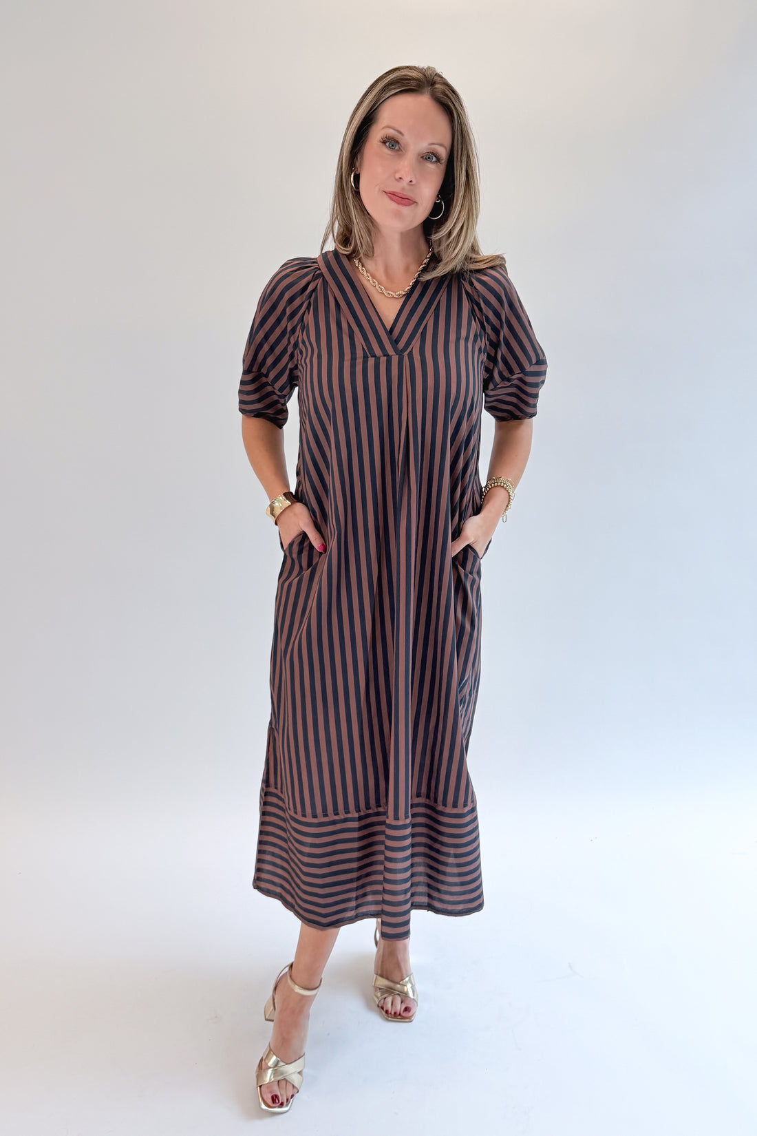 Front view of woman wearing Swagger Boutique’s Navy &amp; Brown Striped Puff Sleeve Midi Dress by Entro with heels against white studio background.