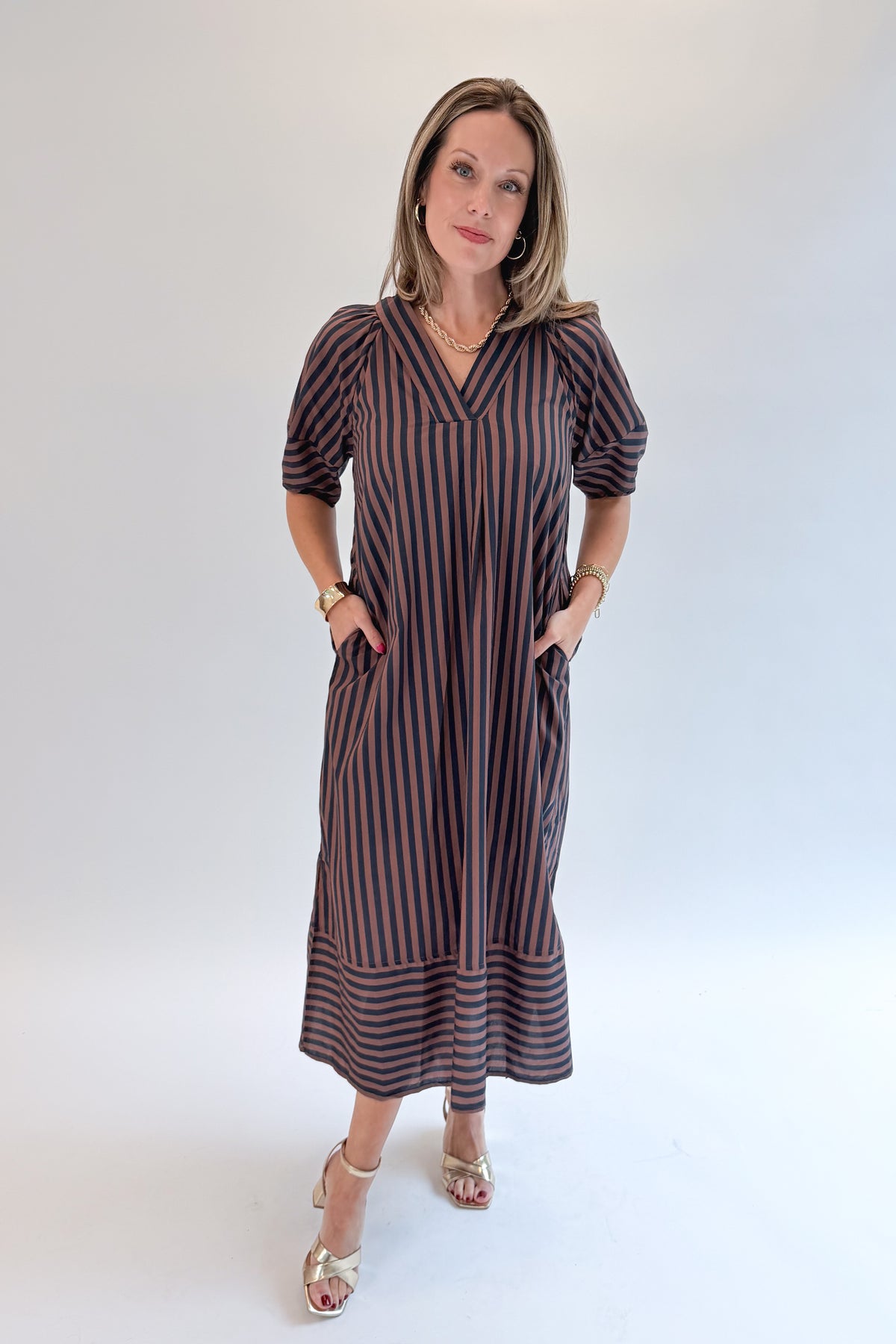 Front view of woman wearing Swagger Boutique’s Navy &amp; Brown Striped Puff Sleeve Midi Dress by Entro with heels against white studio background.