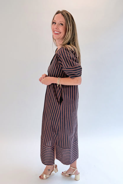 Side view of woman wearing Swagger Boutique’s Navy &amp; Brown Striped Puff Sleeve Midi Dress by Entro with heels against white studio background.