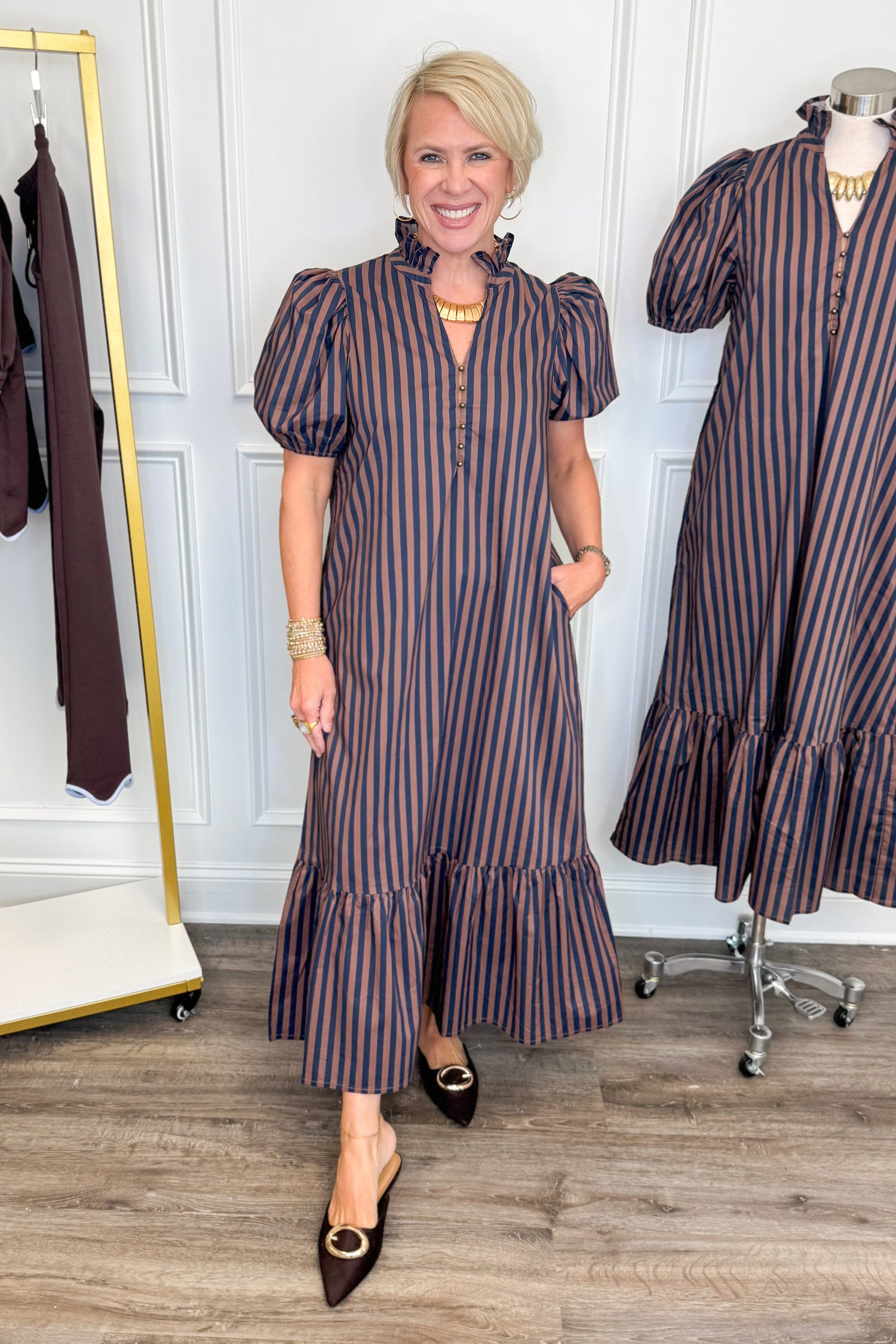 Front view of woman wearing Swagger Boutique’s Navy &amp; Brown Striped Puff Sleeve Midi Dress by Entro with clothing hanging in the background.