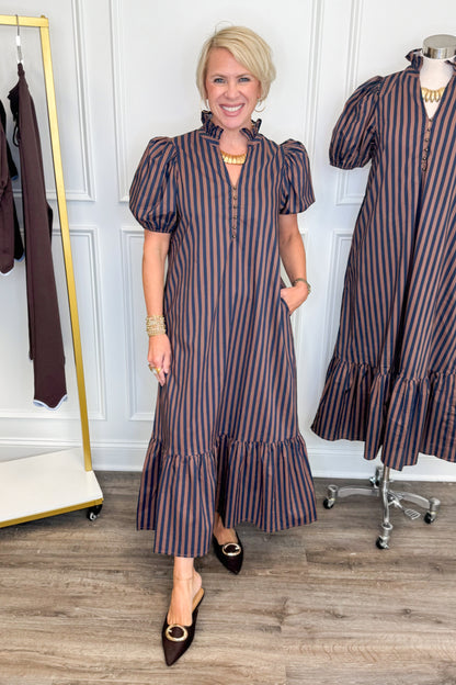 Front view of woman wearing Swagger Boutique’s Navy &amp; Brown Striped Puff Sleeve Midi Dress by Entro with clothing hanging in the background.