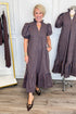 Front view of woman wearing Swagger Boutique’s Navy & Brown Striped Puff Sleeve Midi Dress by Entro with clothing hanging in the background.