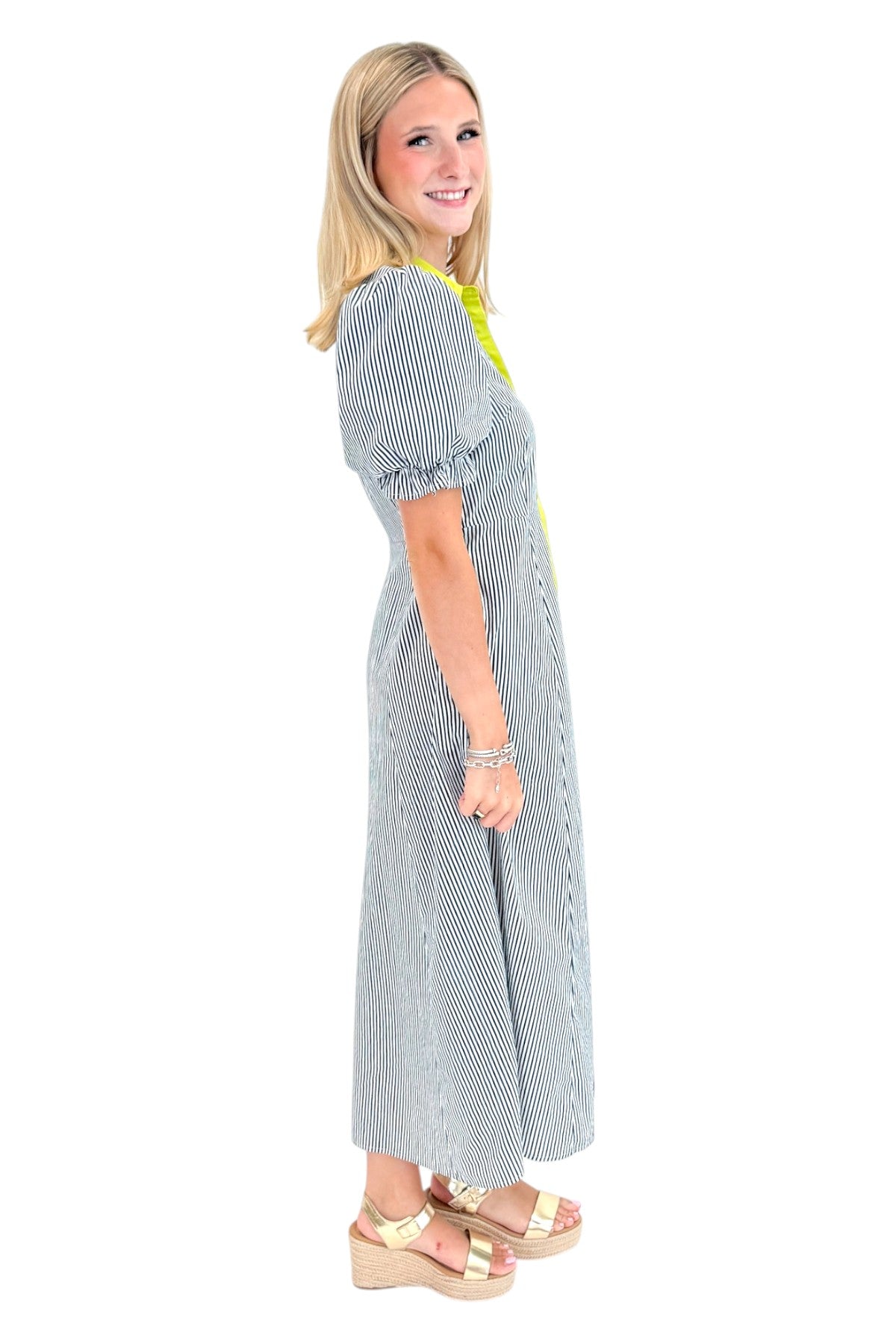 Side view of woman wearing Swagger Boutique’s Navy &amp; Citron Striped Midi Dress by Entro with sandals against white studio background.