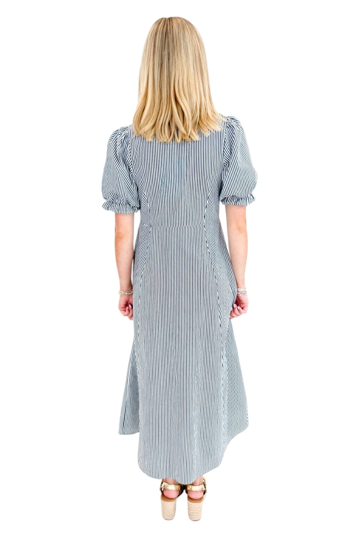 Back view of woman wearing Swagger Boutique’s Navy &amp; Citron Striped Midi Dress by Entro with sandals against white studio background.