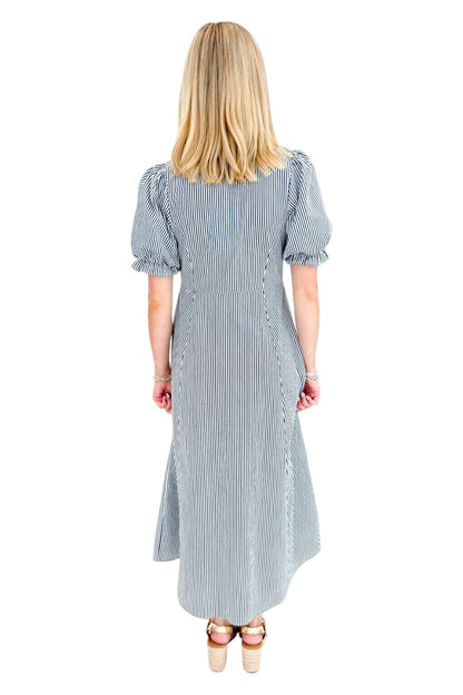 Back view of woman wearing Swagger Boutique’s Navy &amp; Citron Striped Midi Dress by Entro with sandals against white studio background.