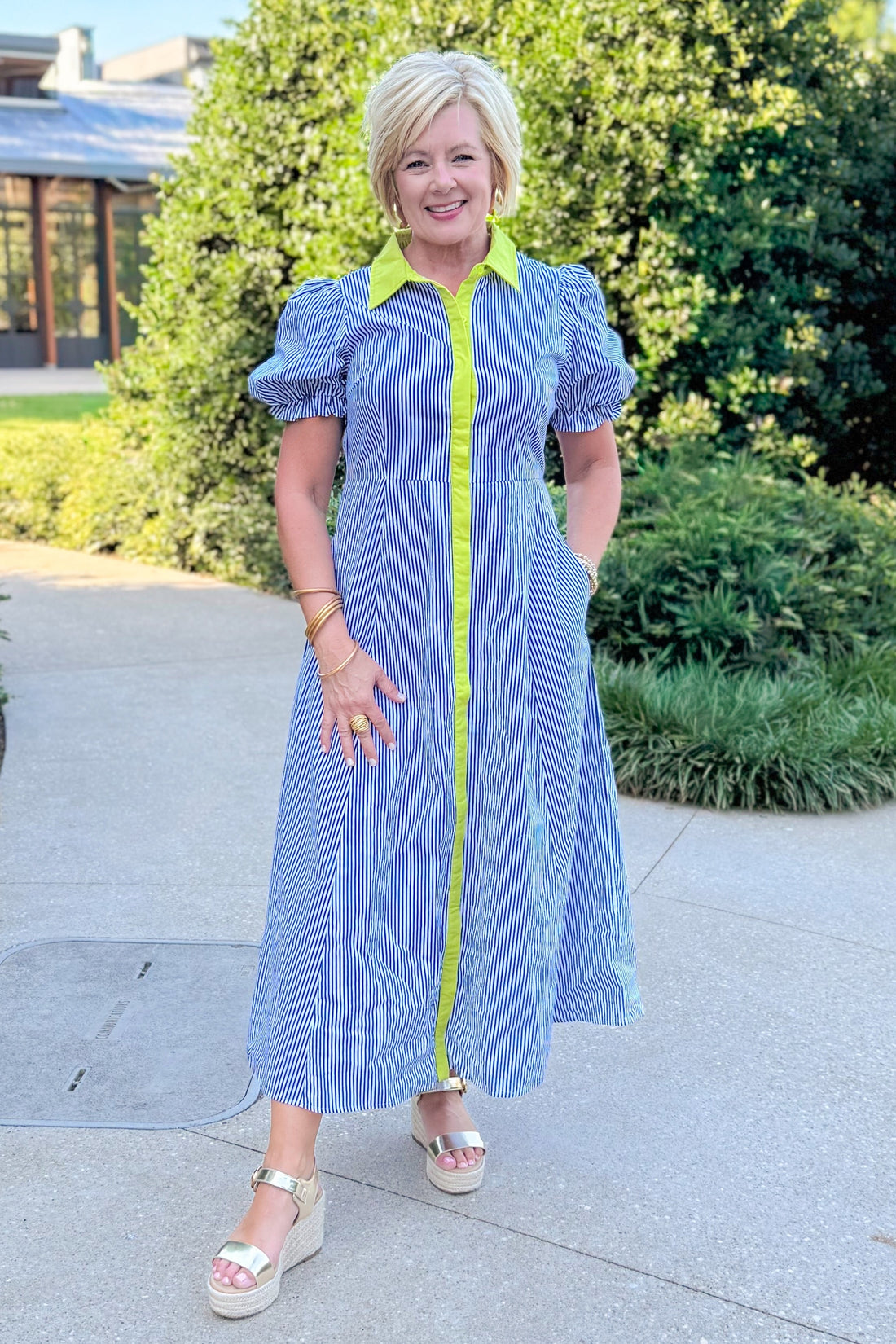 Front view of woman wearing Swagger Boutique’s Navy &amp; Citron Striped Midi Dress by Entro with sandals standing outside at a park.