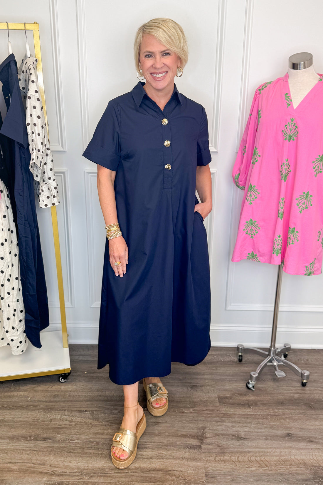 Front view of woman wearing Swagger Boutique’s Navy Collared Midi Dress by Entro with platform sandals with clothes near her. 