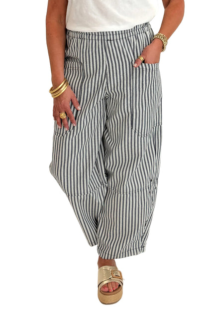 Front detail view of woman wearing Swagger Boutique’s In Full Swing Navy &amp; Cream Striped Barrel Pants with white top and sandals against white studio background.