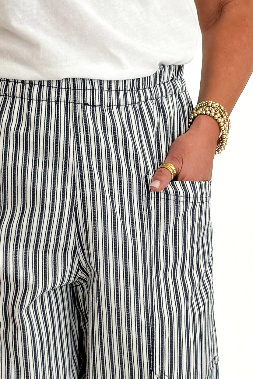 Front detail view of woman wearing Swagger Boutique’s In Full Swing Navy &amp; Cream Striped Barrel Pants with white top and sandals against white studio background.