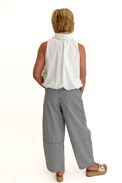 Back view of woman wearing Swagger Boutique’s In Full Swing Navy &amp; Cream Striped Barrel Pants with white top and sandals against white studio background.