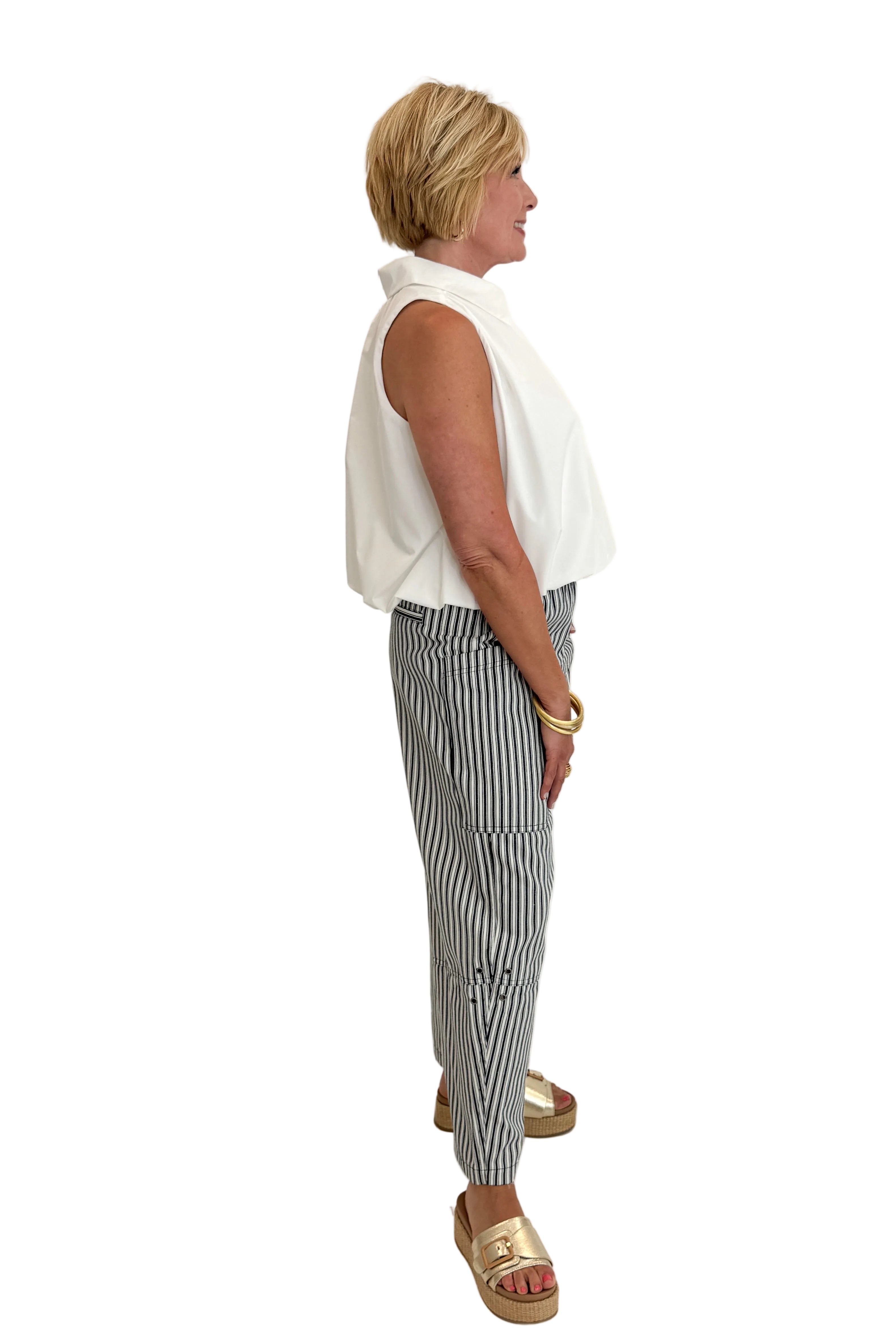 Side view of woman wearing Swagger Boutique’s In Full Swing Navy &amp; Cream Striped Barrel Pants with white top and sandals against white studio background.