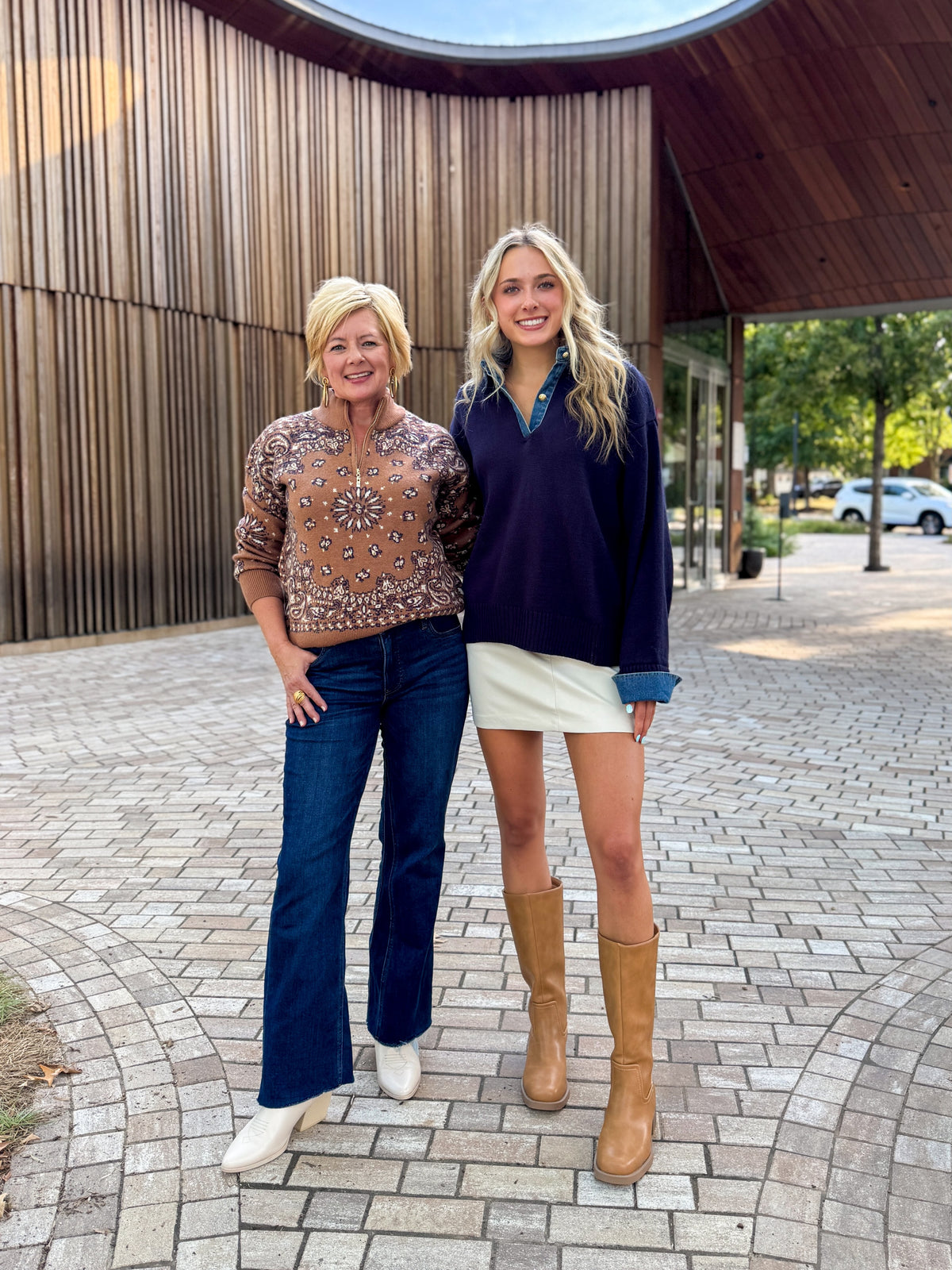 Front view of women wearing Swagger Boutique’s Camel Bandana Print Half Zip Sweater and Navy &amp; Denim Sweater with jeans standing outside on a brick path.