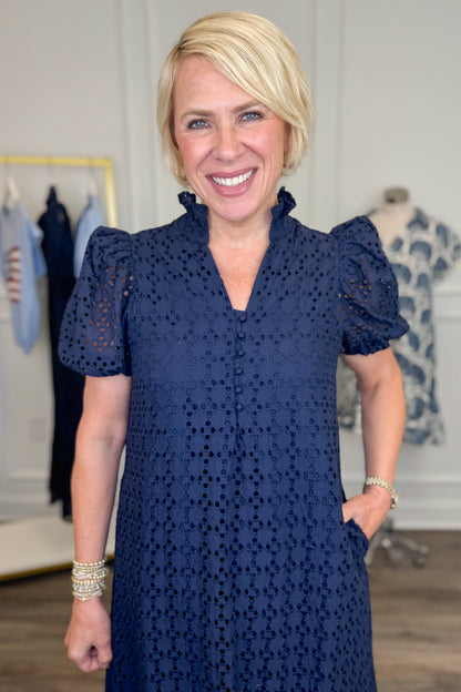 Front detail view of woman wearing Swagger Boutique’s Navy Eyelet Midi Dress by Entro with sandals against white studio background.