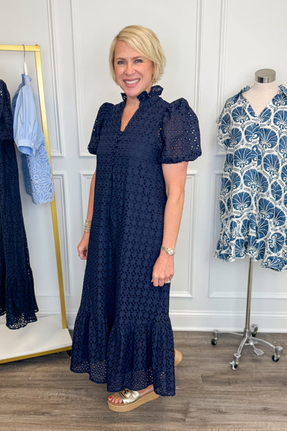 Side detail view of woman wearing Swagger Boutique’s Navy Eyelet Midi Dress by Entro with sandals against white studio background.
