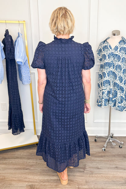 Back detail view of woman wearing Swagger Boutique’s Navy Eyelet Midi Dress by Entro with sandals against white studio background.