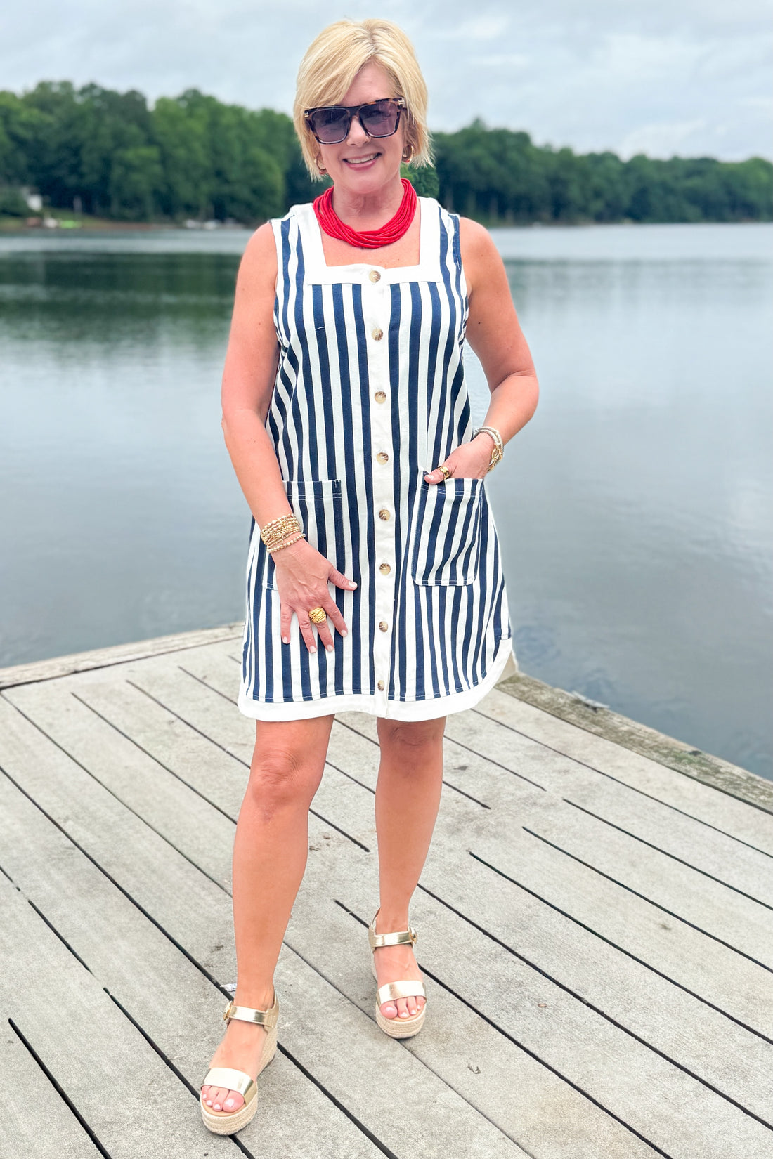 Front view of woman wearing Swagger Boutique’s Navy &amp; White Striped Button Up Mini Dress by Entro with sandals outside at the lake.