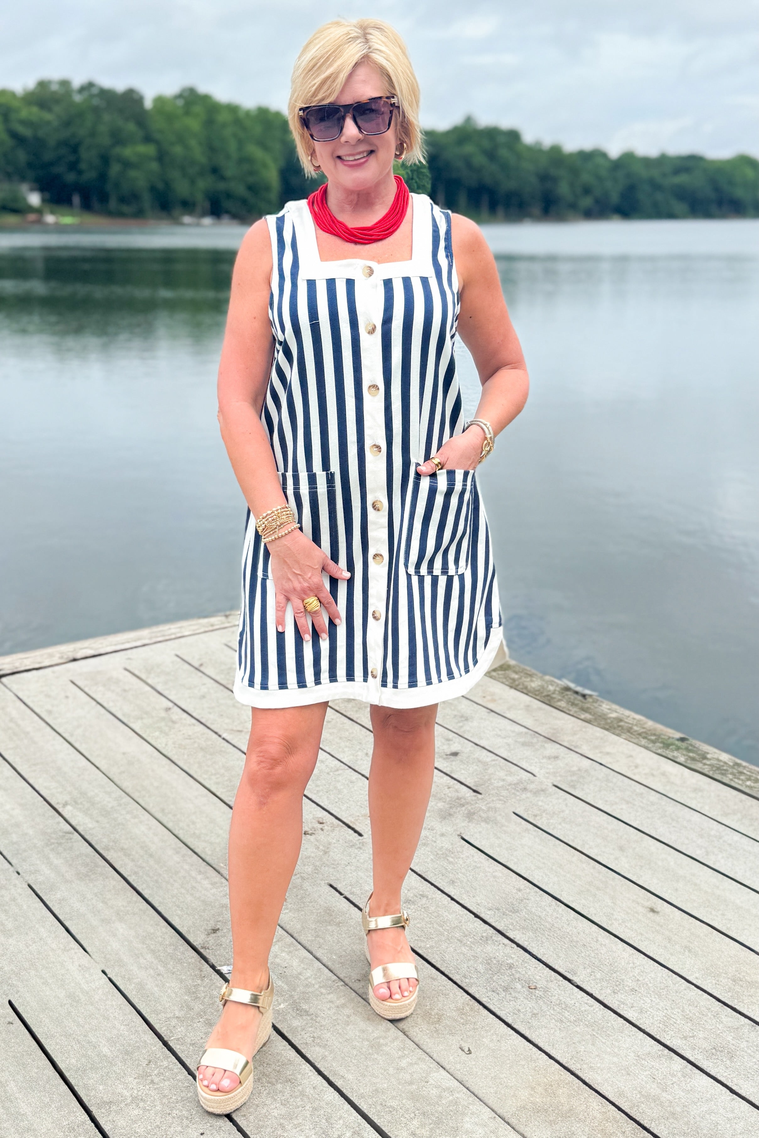 Front view of woman wearing Swagger Boutique’s Navy &amp; White Striped Button Up Mini Dress by Entro with sandals outside at the lake.