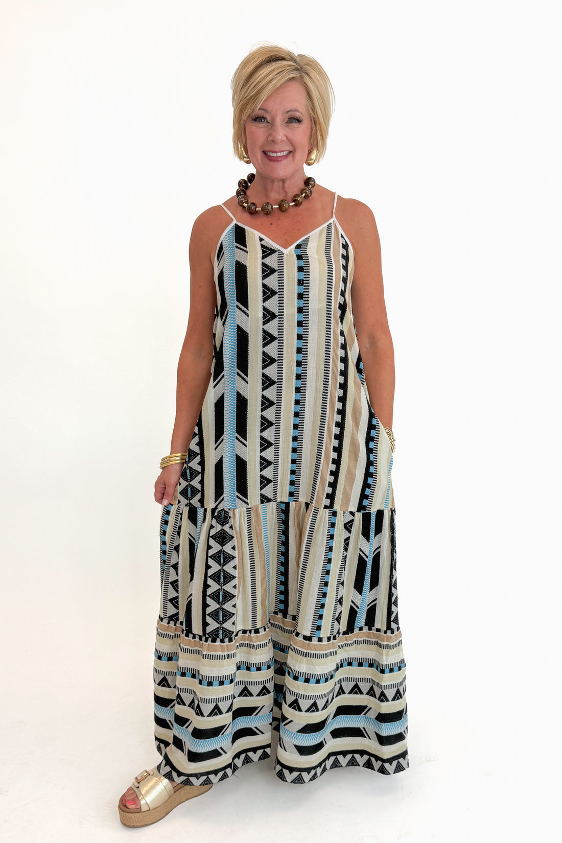 Front view of woman wearing Swagger Boutique’s Neutral Aztec Print Maxi Dress with sandals against white studio background.