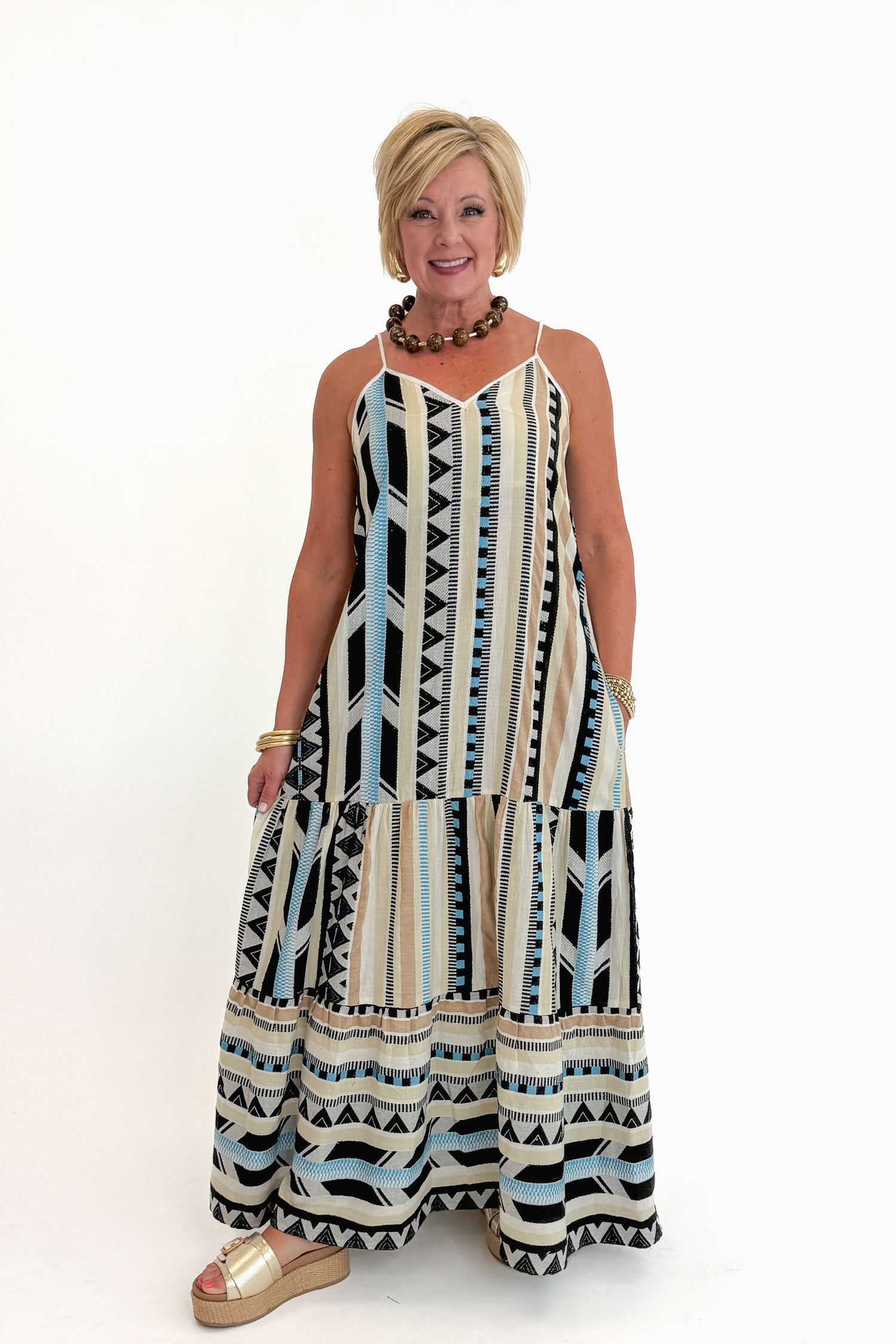 Front view of woman wearing Swagger Boutique’s Neutral Aztec Print Maxi Dress with sandals against white studio background.