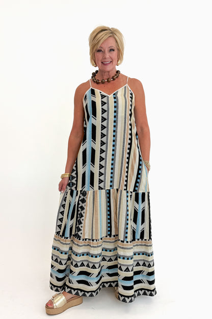 Front view of woman wearing Swagger Boutique’s Neutral Aztec Print Maxi Dress with sandals against white studio background.