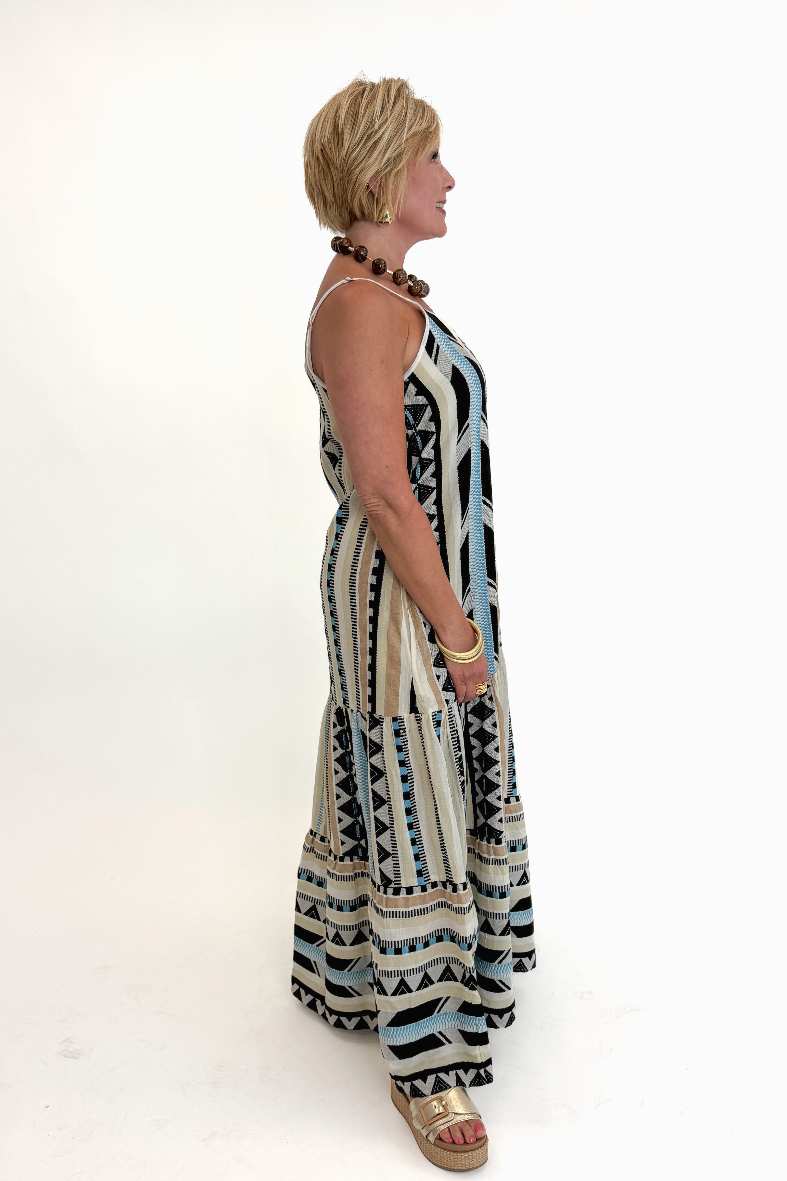 Side view of woman wearing Swagger Boutique’s Neutral Aztec Print Maxi Dress with sandals against white studio background.