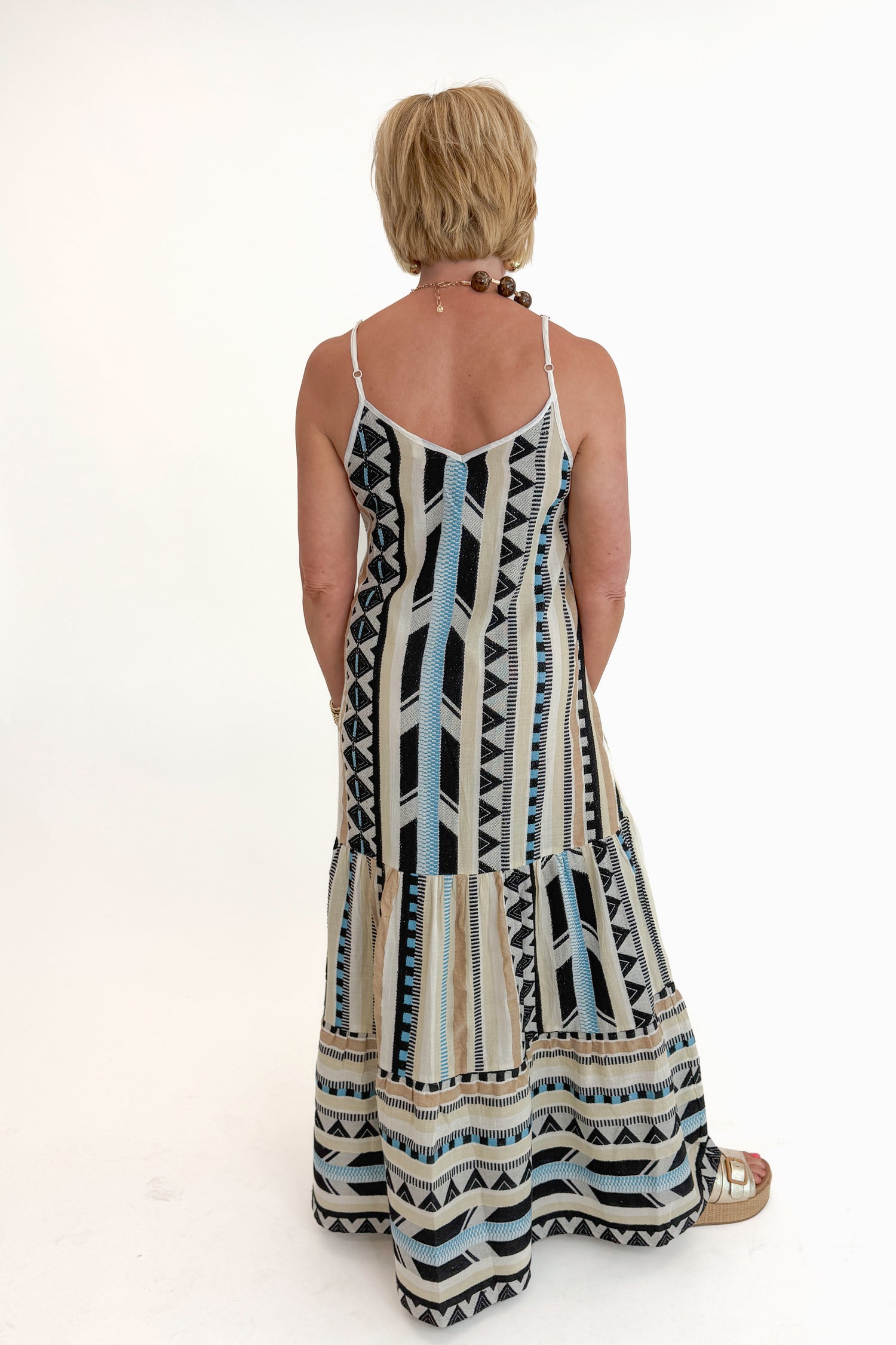 Back view of woman wearing Swagger Boutique’s Neutral Aztec Print Maxi Dress with sandals against white studio background.