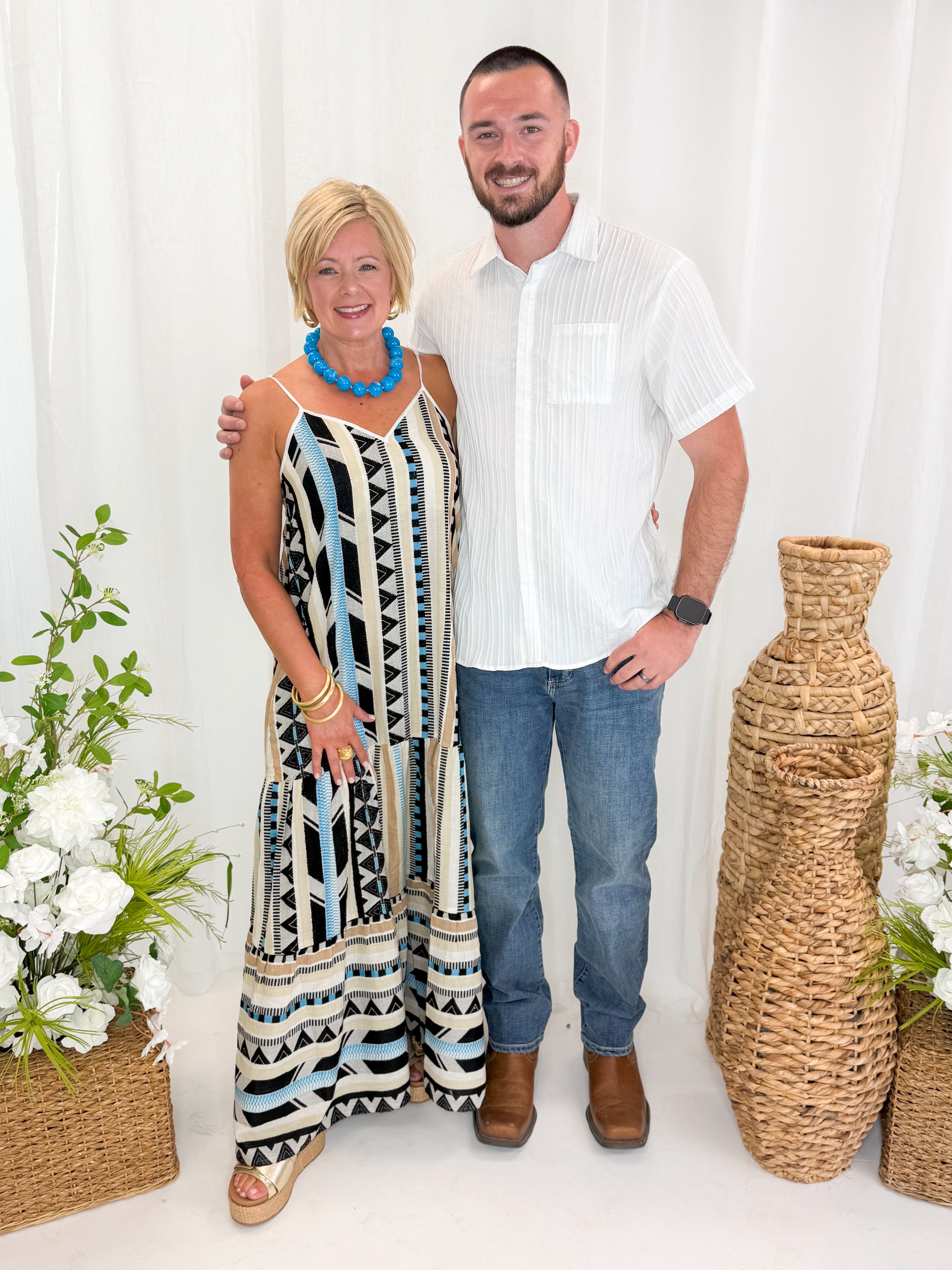 Front view of woman wearing Swagger Boutique’s Neutral Aztec Print Maxi Dress with sandals and son against decorative background.