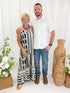 Front view of woman wearing Swagger Boutique’s Neutral Aztec Print Maxi Dress with sandals and son against decorative background.