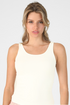 A woman modeling a sleeveless scoop-neck tank top in a solid ivory color, paired with a light pink ruffled skirt, against a light gray studio background.