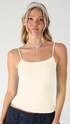 A woman wearing a light cream spaghetti-strap camisole top, a silver beaded headband, and a silver choker necklace, paired with dark navy bottoms, against a plain light gray background.