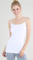 A smiling blonde woman wearing a white spaghetti-strap camisole tank top and light-wash jeans, standing against a plain light gray studio background.