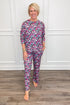 Model wearing the No Peeking Navy Annie Pajama Set, featuring a colorful Christmas present print in pink, green, blue, and white on a navy background. The set includes a relaxed-fit, long-sleeve crewneck top and matching straight-leg pajama pants with side pockets.